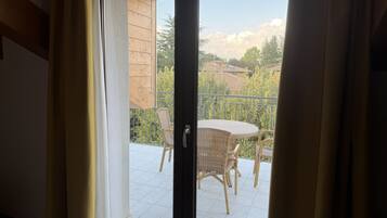 A view through a sliding glass door to an outdoor balcony with wicker furniture and a tiled floor.