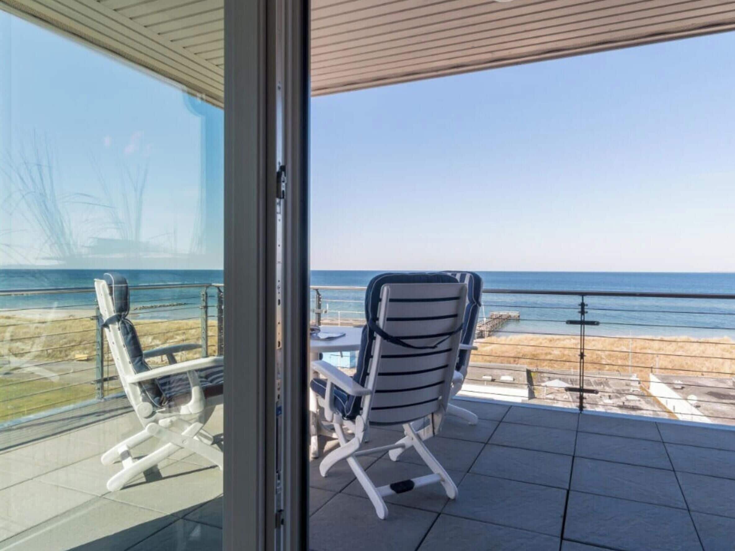 A balcony with a view of the beach, a table, and two chairs.