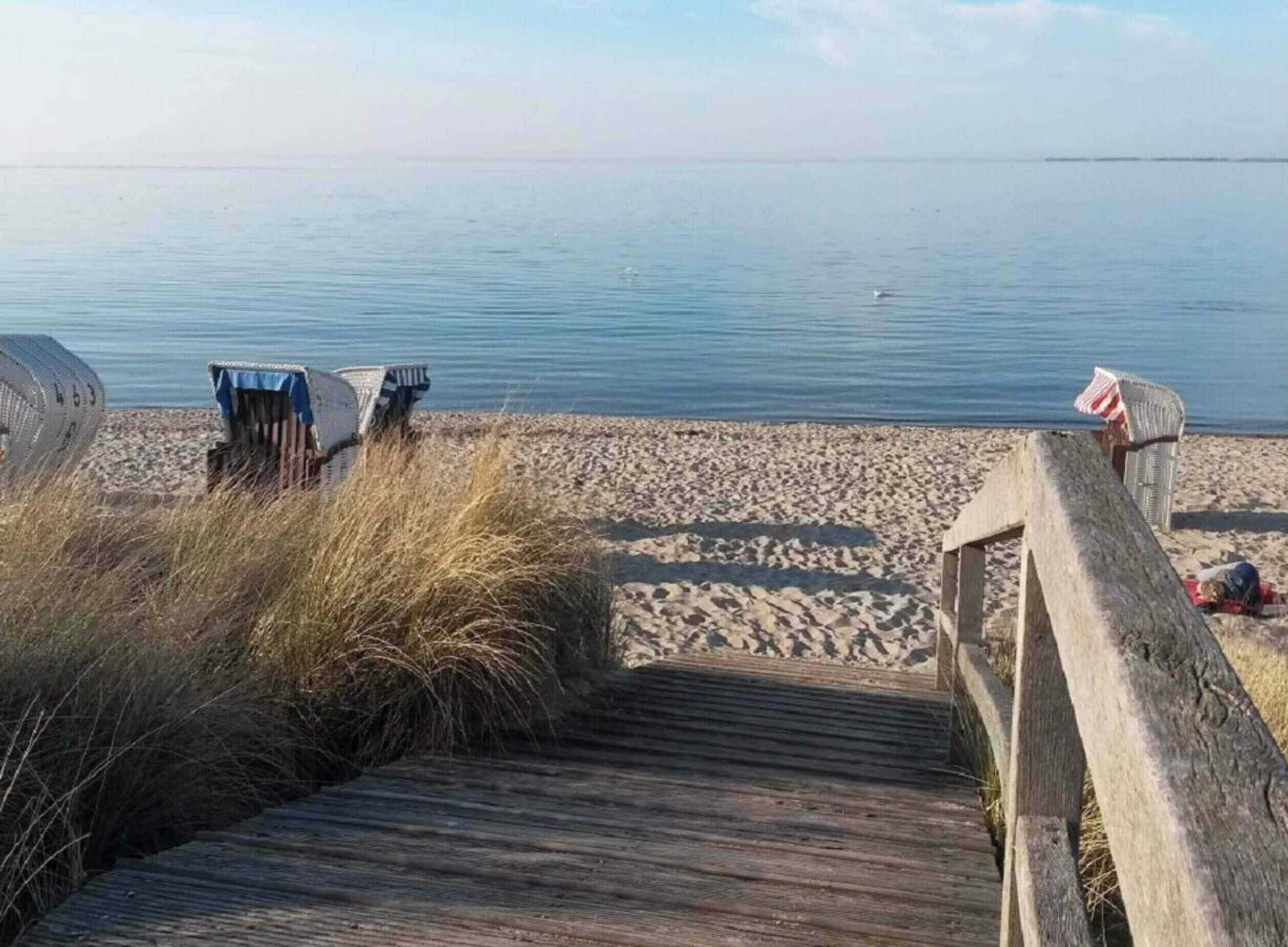 A wooden boardwalk leading to a sandy beach with calm water in the background.