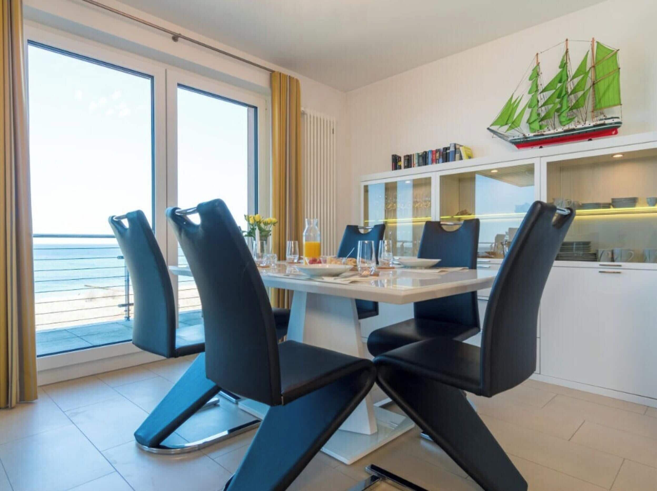 Ein moderner Essbereich mit einem Tisch für vier Personen, schwarzen Stühlen und Meerblick durch große Fenster.