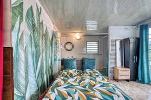 Ein Schlafzimmer mit einem Bett, einem Schminktisch, einem Spiegel und einer Wand mit Blätermotiv.