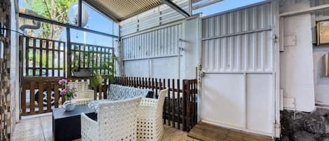 A covered outdoor seating area with wicker furniture, a tiled floor, and a metal gate.