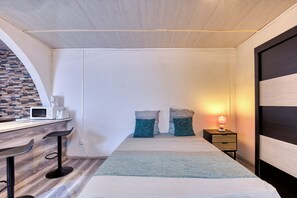 A compact room with a kitchenette, a bed with pillows, a bedside table with a lamp, and a wooden floor. - Petit Salomon - Jardin - Proche plage (Saint-Pierre)