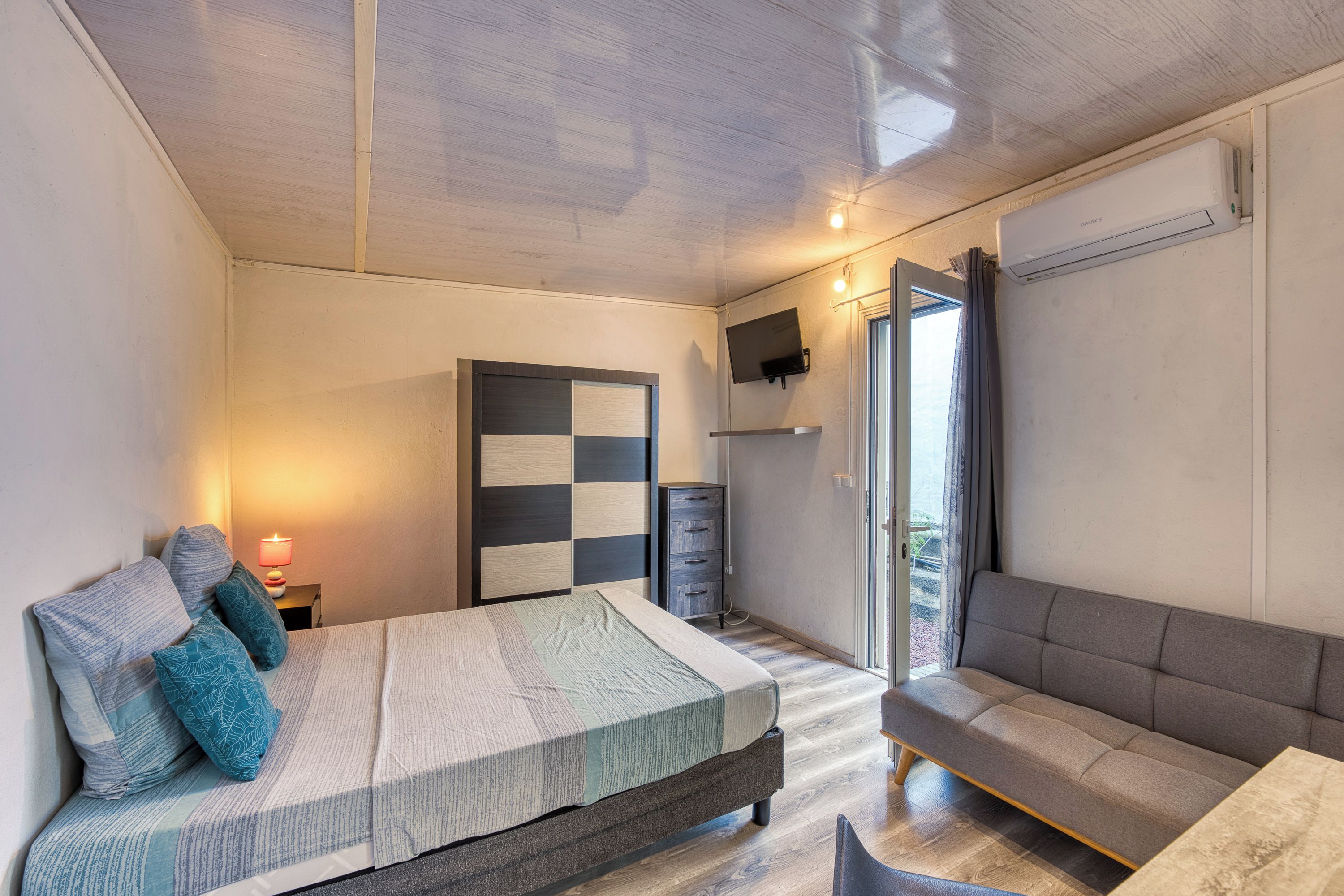 Een slaapkamer met een bed, een bank, een televisie en een raam.