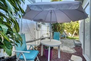 A patio area with a round table, two chairs, a large umbrella, and a trash bin. - Petit Salomon - Jardin - Proche plage (Saint-Pierre)