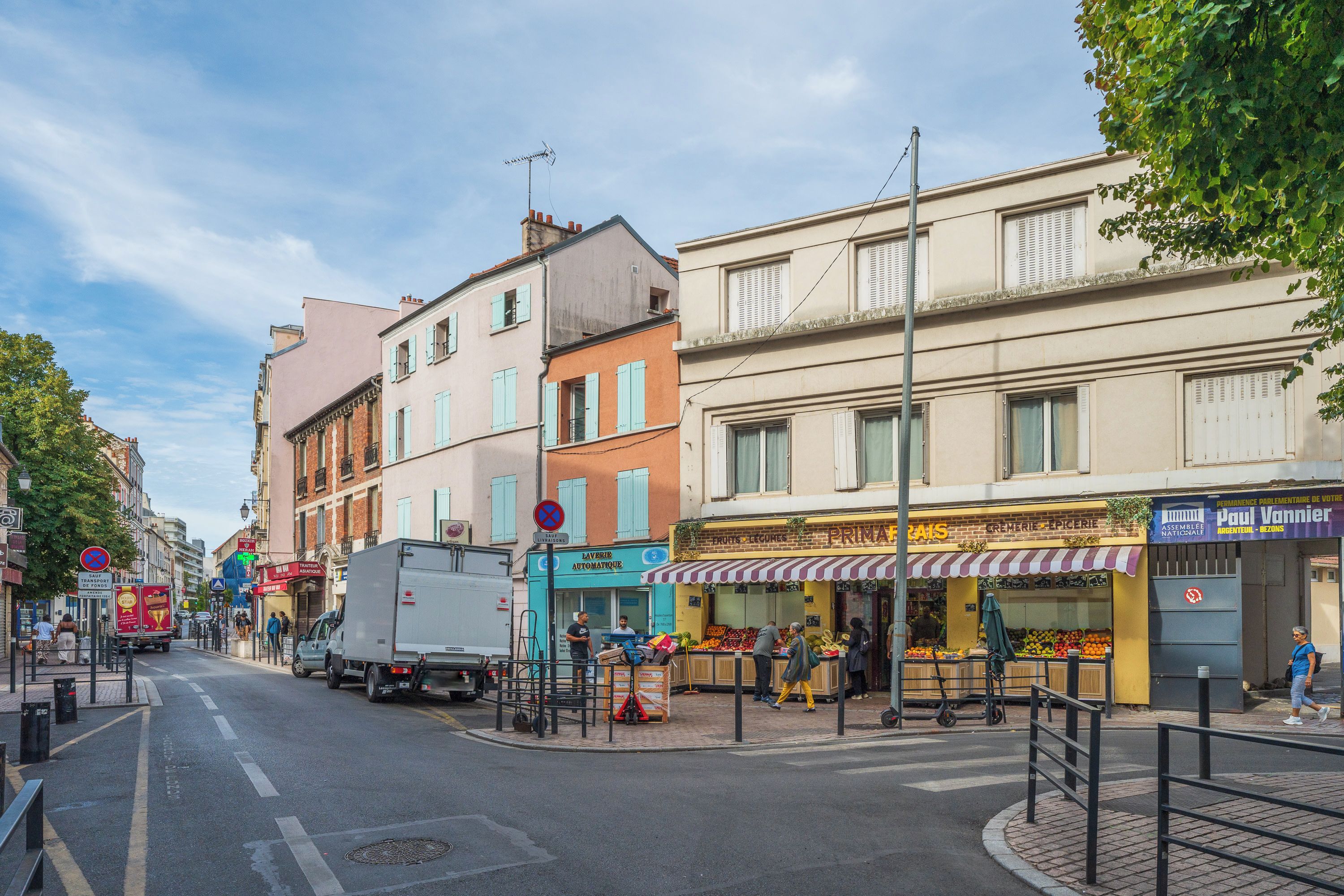 A street view with buildings, a fruit stand, and a truck parked on the side.