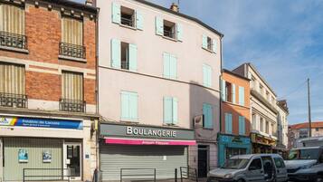 Une vue de rue avec des immeubles, une boulangerie fermée et des voitures garées.