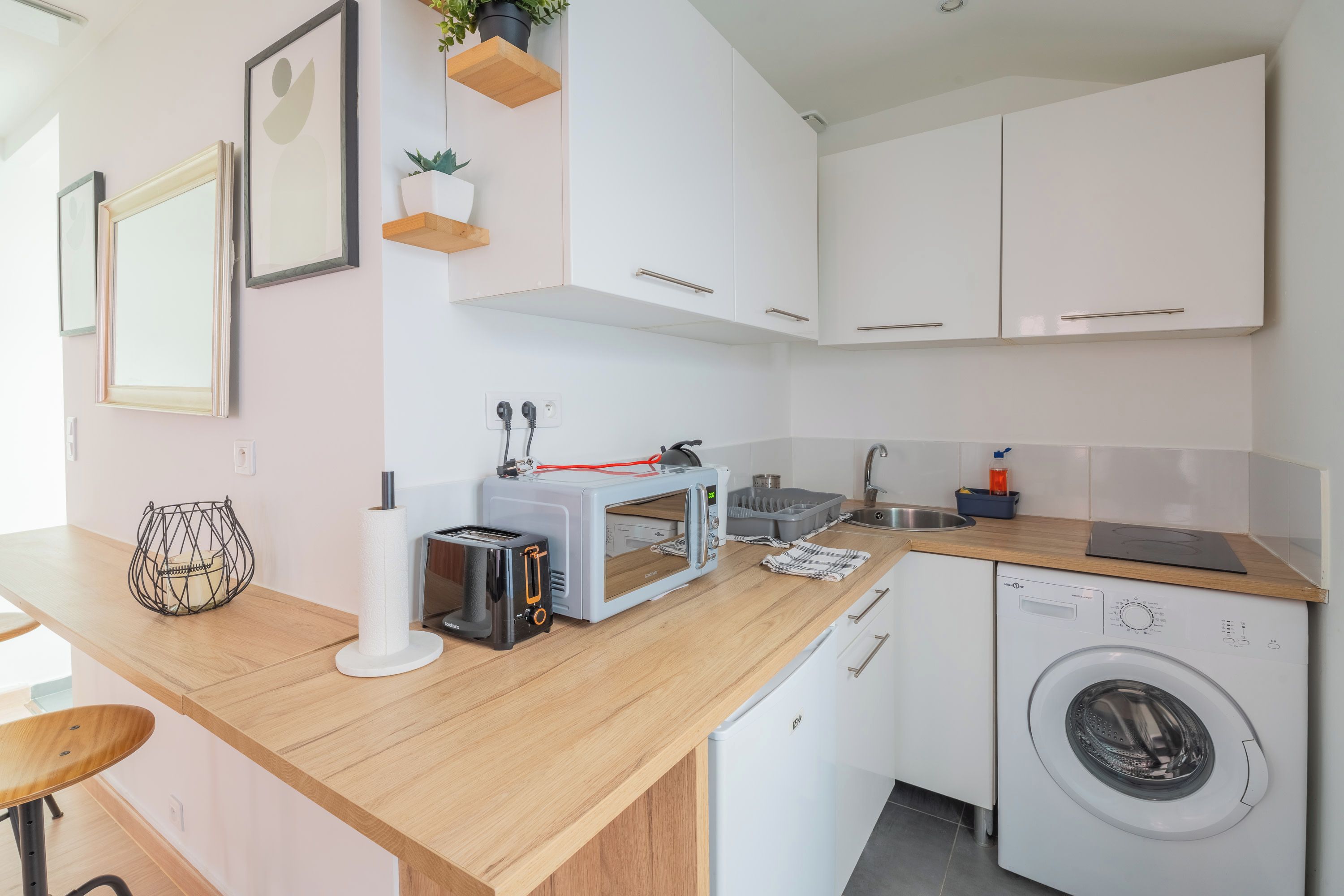 Une cuisine moderne avec des meubles blancs, un plan de travail en bois, un lave-linge et un grille-pain.