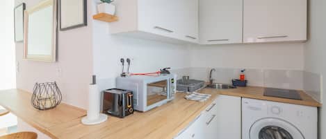 Une cuisine moderne avec des meubles blancs, un plan de travail en bois, un lave-linge et un grille-pain.
