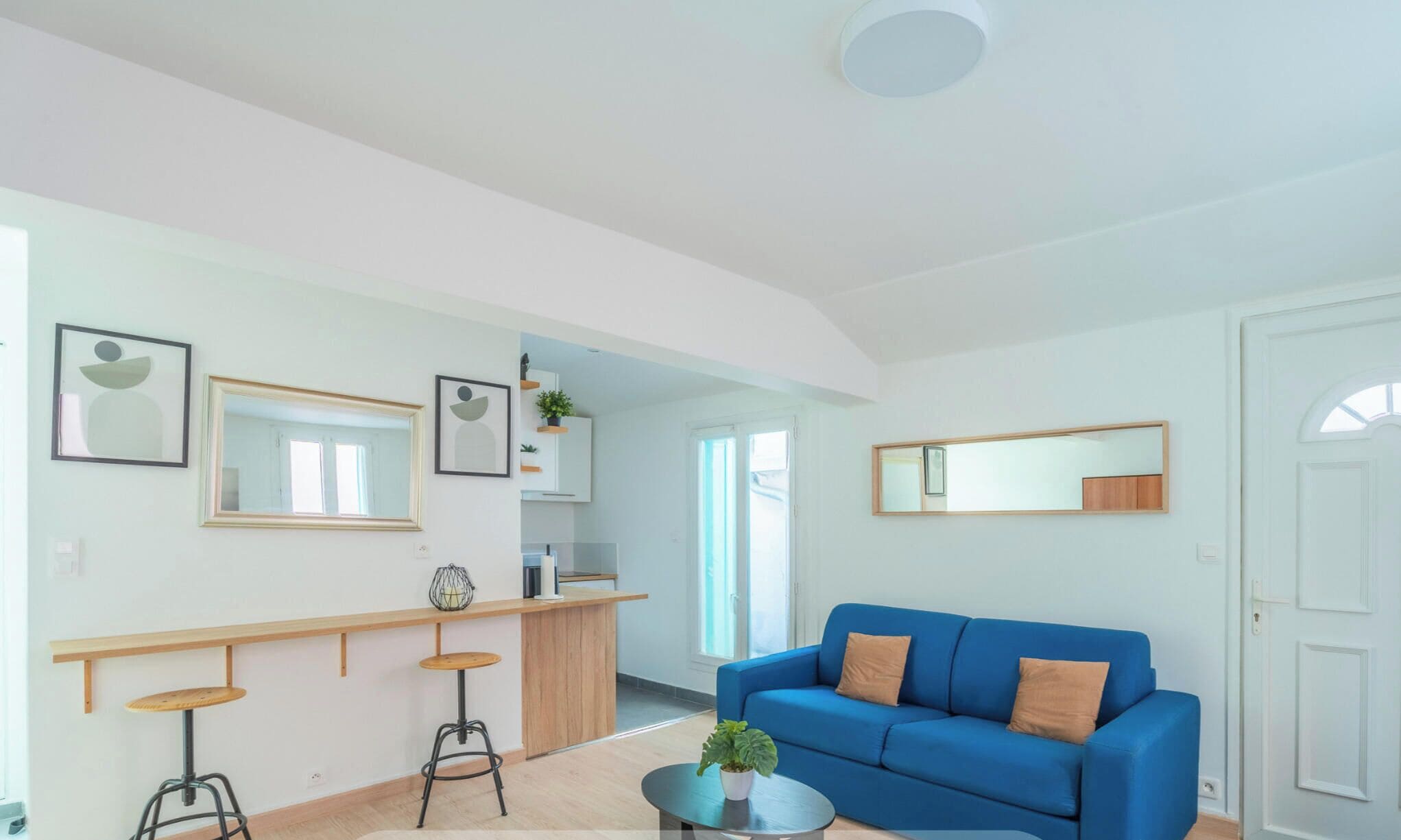 A modern living room with a blue sofa, a kitchen area with a wooden countertop, and a dining bar with stools.