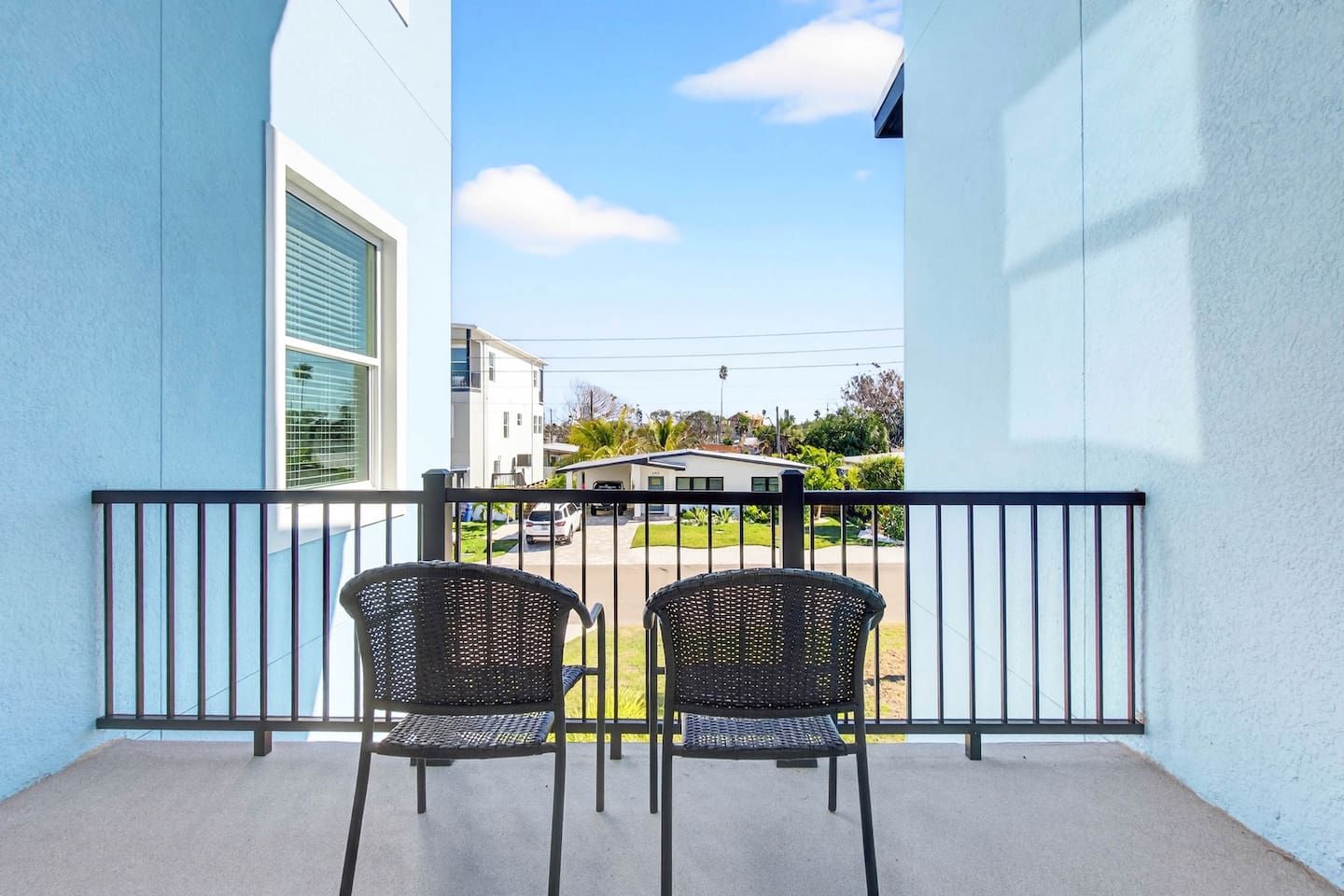 A balcony with two wicker chairs and a metal railing, overlooking a residential street.