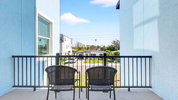 A balcony with two wicker chairs and a metal railing, overlooking a residential street.