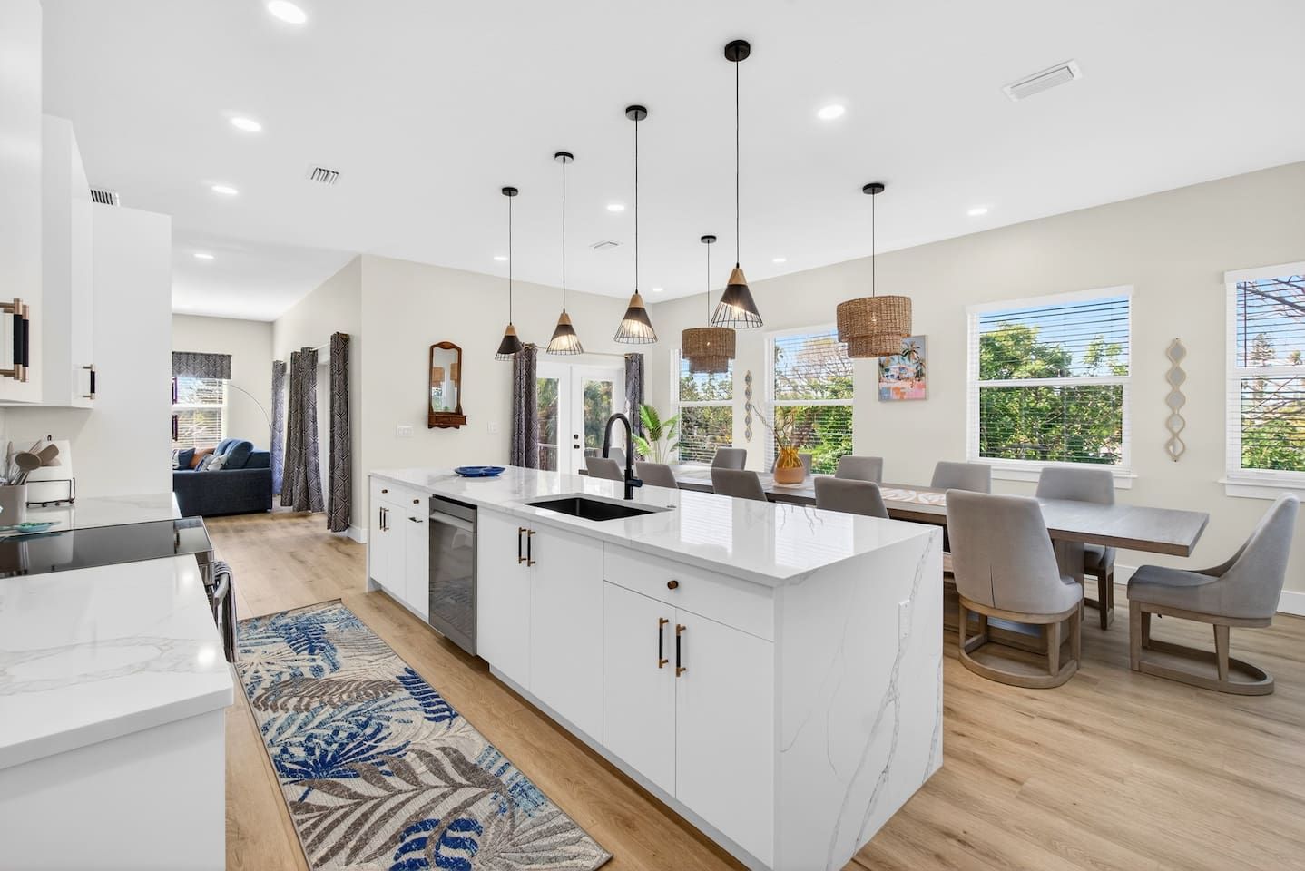 Una cocina moderna con armarios blancos, una isla central, iluminación colgante y una zona de comedor con mesa y sillas.