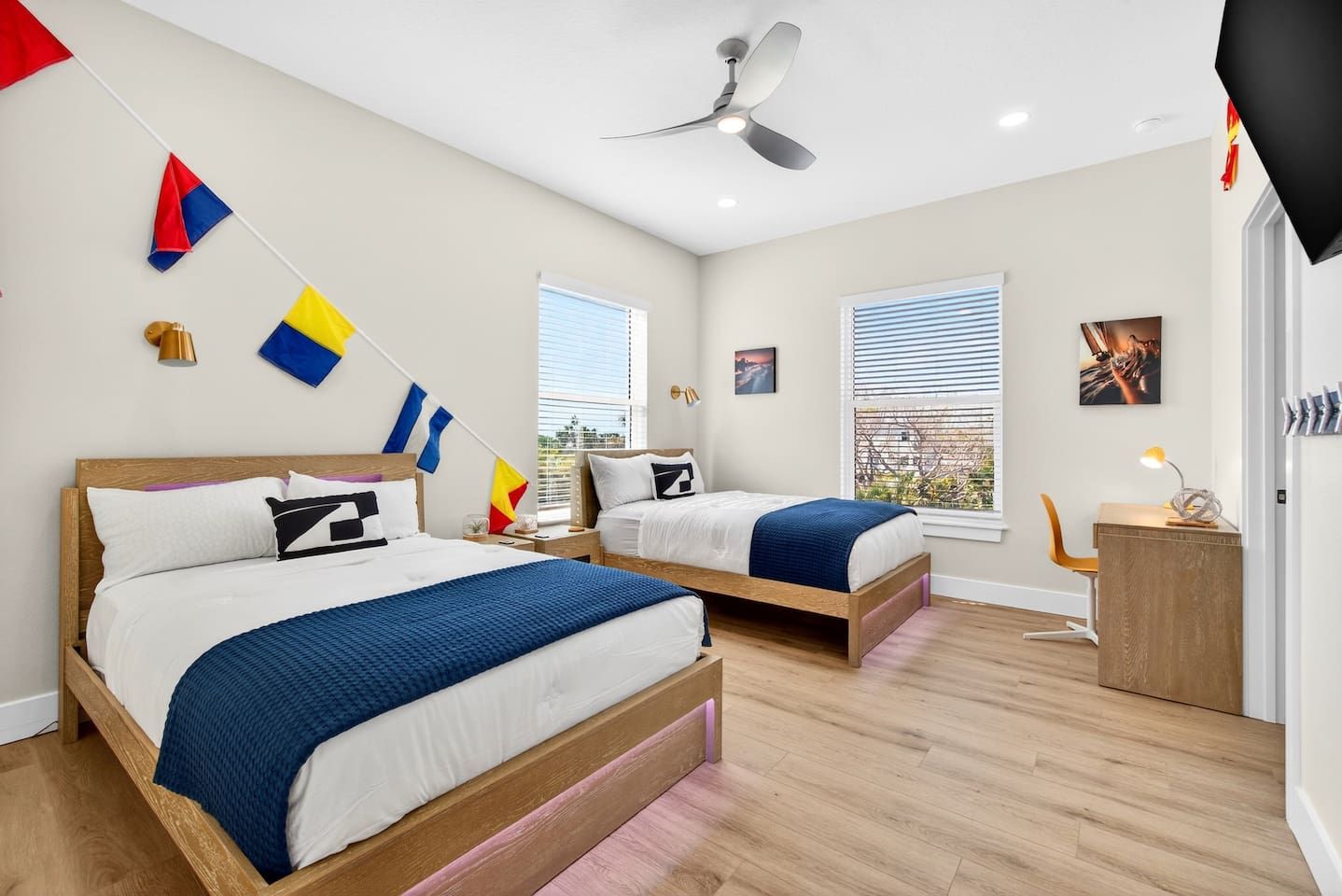 Quarto com duas camas, ventoinha no teto e escrivaninha com abajur.