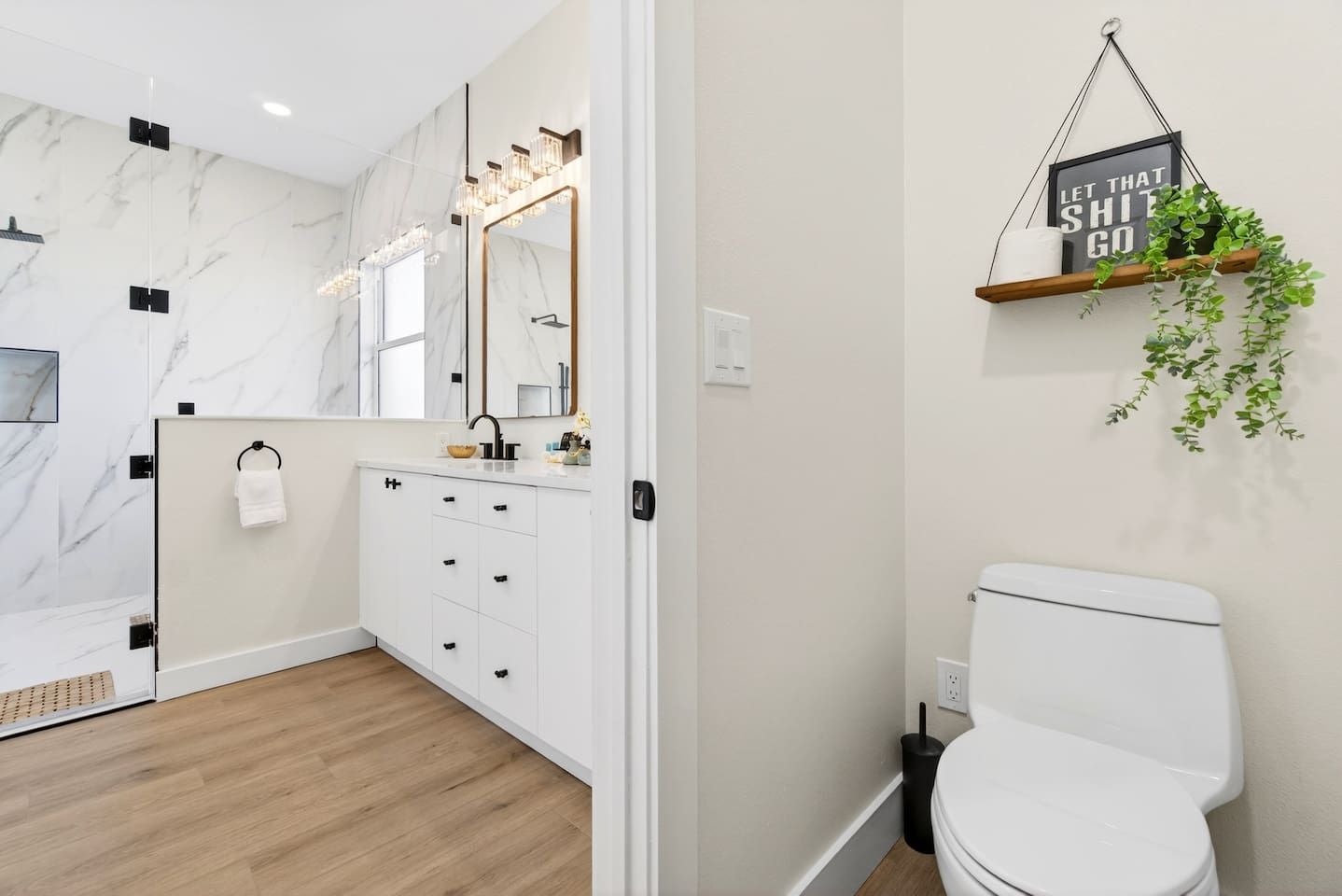A modern bathroom with a marble wall, a white sink with a gold faucet, and a toilet.