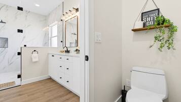 A modern bathroom with a marble wall, a white sink with a gold faucet, and a toilet.