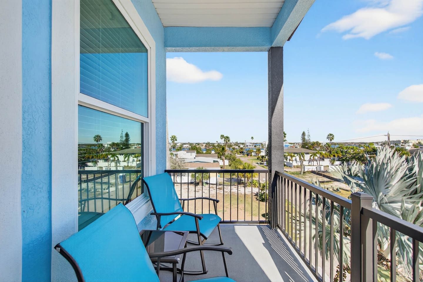 A balcony with two chairs and a table, overlooking a residential area with palm trees and houses.