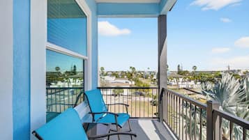 A balcony with two chairs and a table, overlooking a residential area with palm trees and houses.