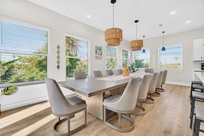 A modern dining area with a long table, multiple chairs, and pendant lighting.