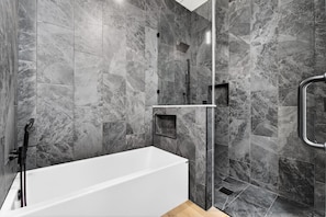 A modern bathroom with a white bathtub, a glass shower enclosure, and marble walls.