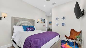 A modern bedroom with a bed, a ceiling fan, wall-mounted artwork, and a flat-screen TV.