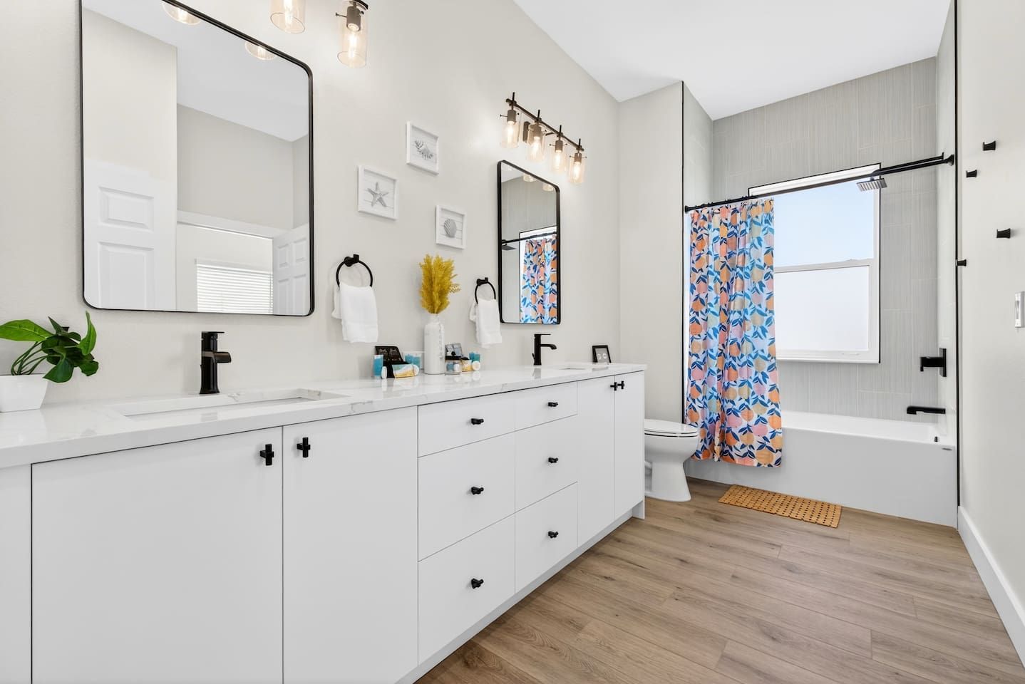 Une salle de bain moderne avec un meuble-lavabo blanc, un grand miroir et une douche agrémentée d’un rideau coloré.