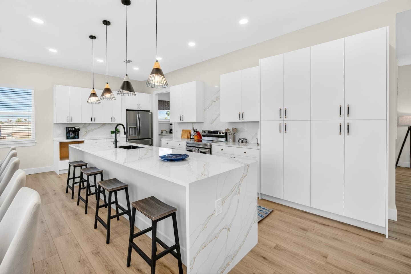 A modern kitchen with white cabinets, a marble island, and pendant lighting.