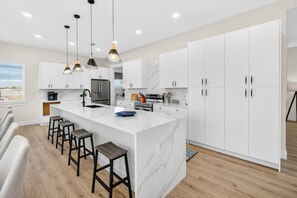 Cocina moderna con armarios blancos, una isla de mármol e iluminación colgante.