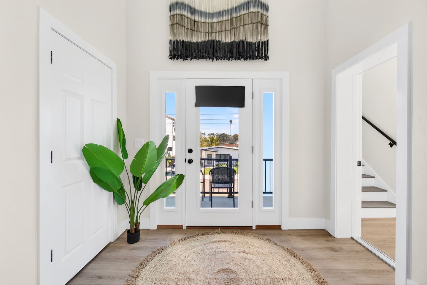 Un couloir avec une porte blanche, une plante en pot, un tapis tissé et un escalier.