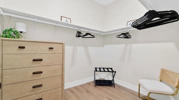 A room with a wooden dresser, a chair, and a small black shelf unit with hanging items.