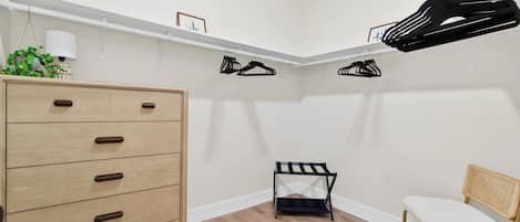 A room with a wooden dresser, a chair, and a small black shelf unit with hanging items.