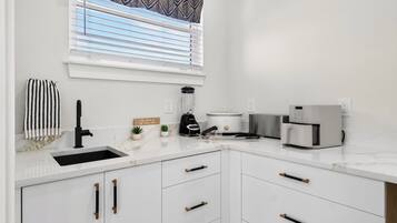 Una cocina moderna con armarios blancos, un grifo negro, una licuadora, una olla de cocción lenta y una cafetera.