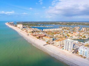 An aerial view of a coastal city with a long sandy beach, dense residential buildings, and a marina.