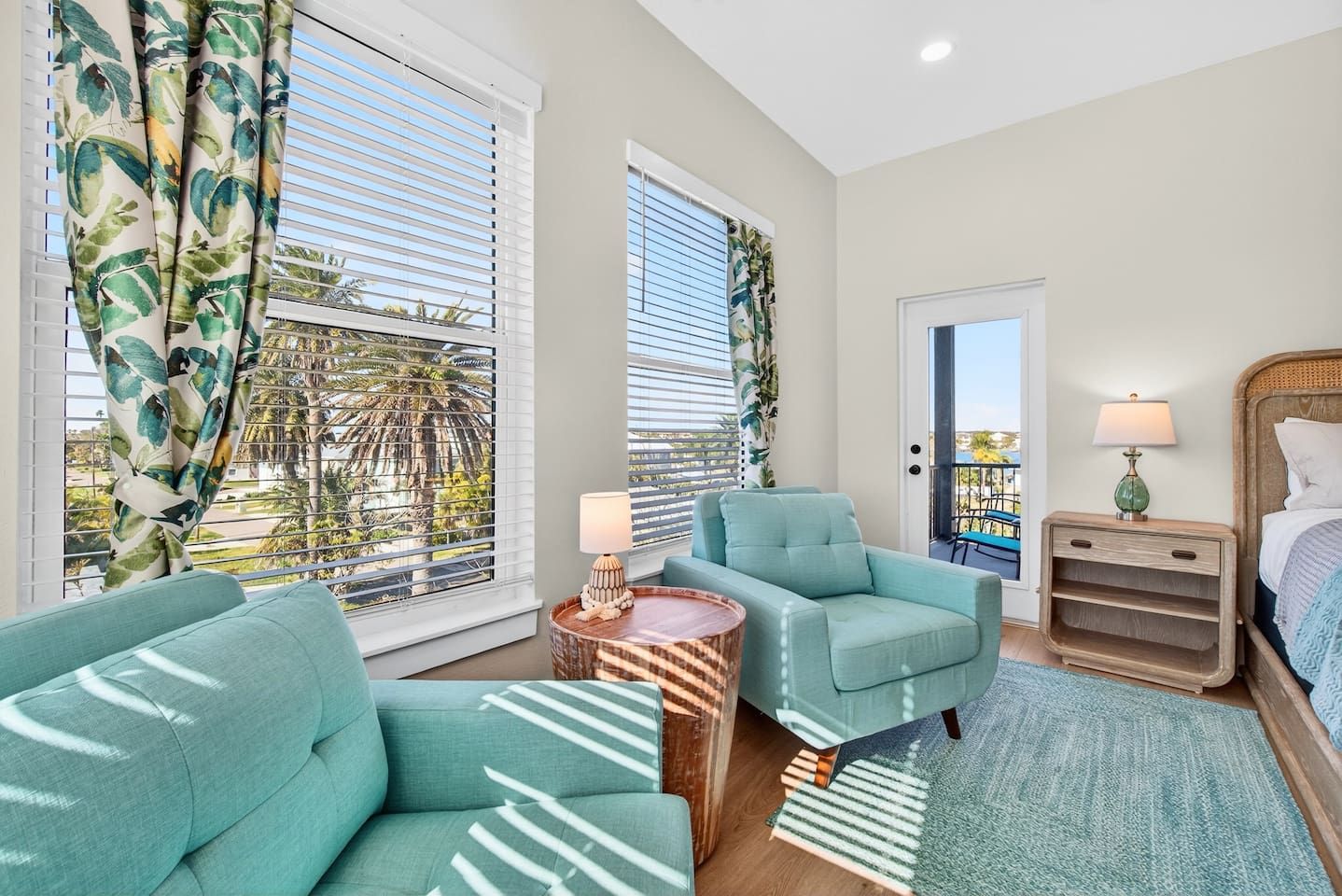 A room with a bed, a nightstand, a lamp, a sofa, a chair, and a window with blinds.