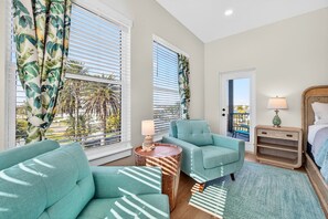 A room with a bed, a nightstand, a lamp, a sofa, a chair, and a window with blinds.