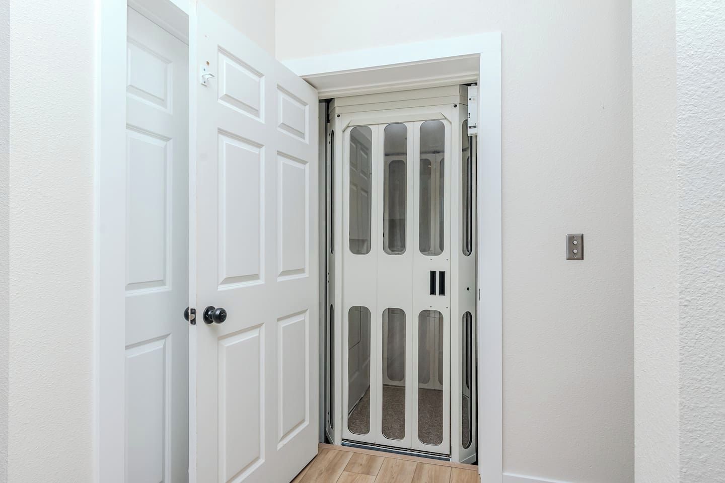A white door with a glass panel, a white wall, and a wooden floor.