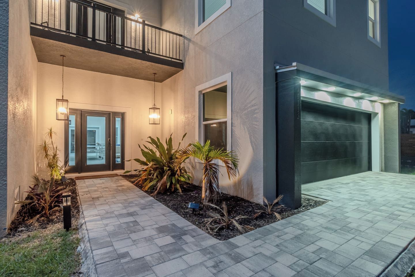 A modern two-story house with a garage, a balcony, and a well-lit entrance.