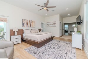 A bedroom with a bed, bedside tables, a ceiling fan, and a view to a balcony.