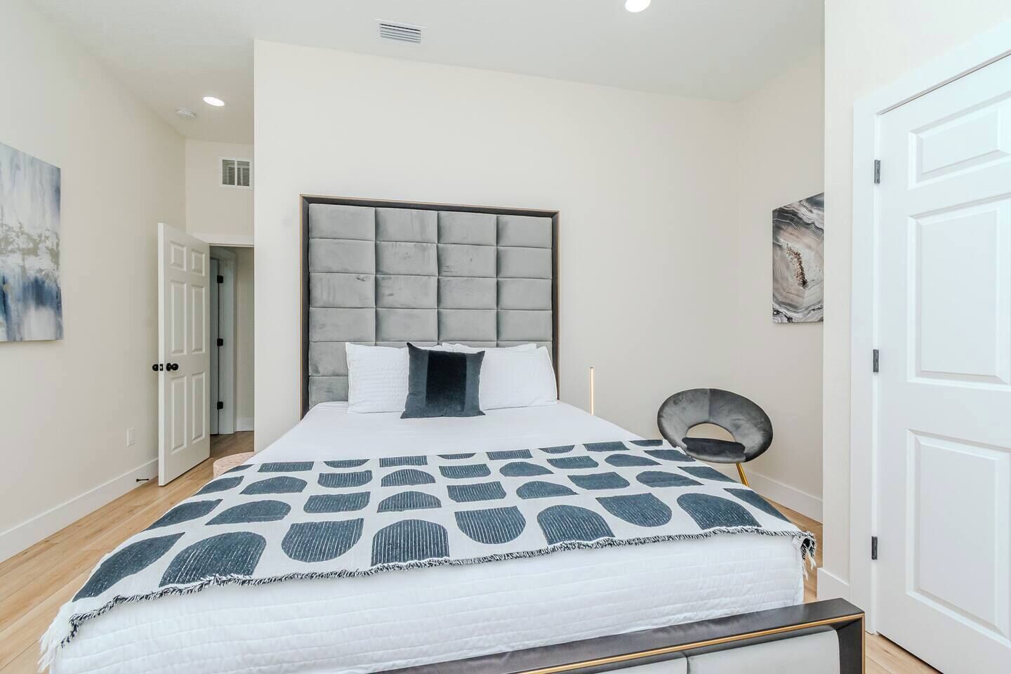 Une chambre à coucher moderne avec un grand lit, une tête de lit capitonnée et une couvre-lit à motifs.