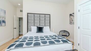 Une chambre à coucher moderne avec un grand lit, une tête de lit capitonnée et une couvre-lit à motifs.