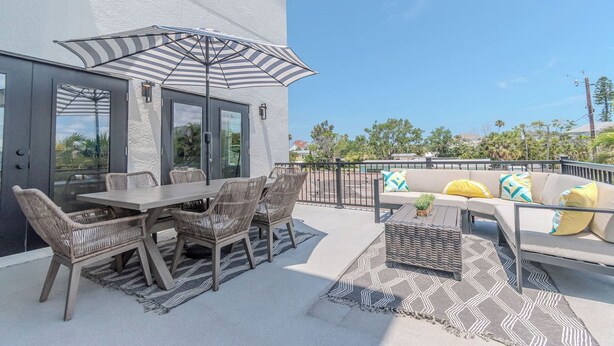 An outdoor patio with a table and chairs, a sofa with cushions, and a striped umbrella. - Spacious Beach Retreat, Sleeps 10 | Walk to Gulf (Redington Beach)