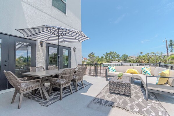 An outdoor patio with a table and chairs, a sofa with cushions, and a striped umbrella.