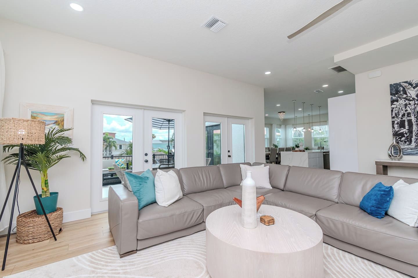 A modern living room with a beige sectional sofa, a round coffee table, and a floor lamp. There is a large window with a view of the outdoors.