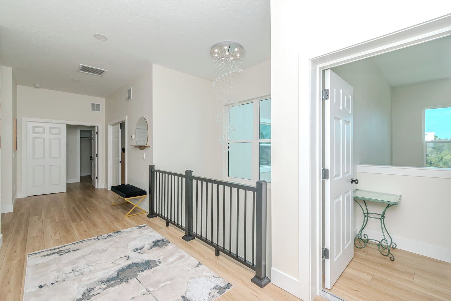 A spacious hallway with a wooden floor, a black railing, and a white door leading to a room with a window.