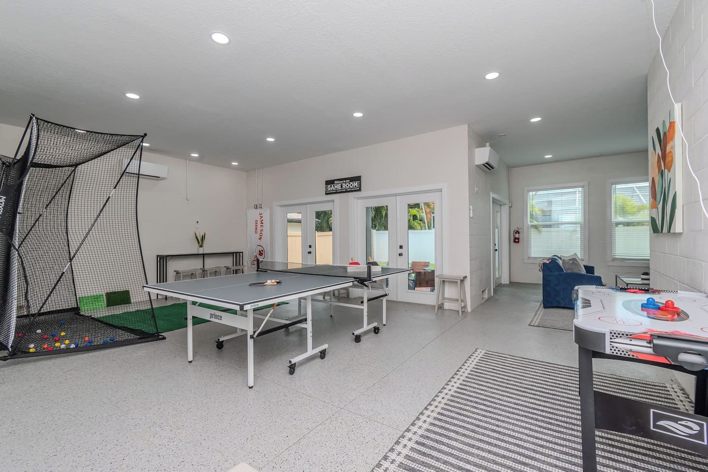 Une pièce équipée d’une table de ping-pong, d’un espace délimité par un filet pour jouer au tennis de table, et d’un jeu de fléchettes.