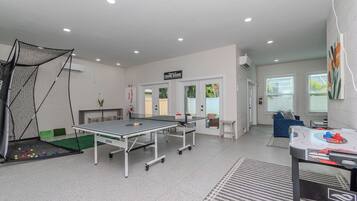 Une pièce équipée d’une table de ping-pong, d’un espace délimité par un filet pour jouer au tennis de table, et d’un jeu de fléchettes.