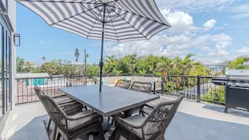 An outdoor patio with a table and chairs, a striped umbrella, and a grill.