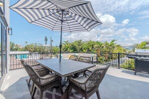 An outdoor patio with a table and chairs, a striped umbrella, and a grill.