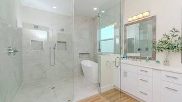 Une salle de bain moderne dotée d’une douche à parois de verre, d’une baignoire sur pieds et d’un meuble-lavabo avec un miroir.