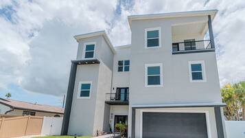A modern multi-story residential building with a garage, a balcony on the upper floor, and a fenced yard.